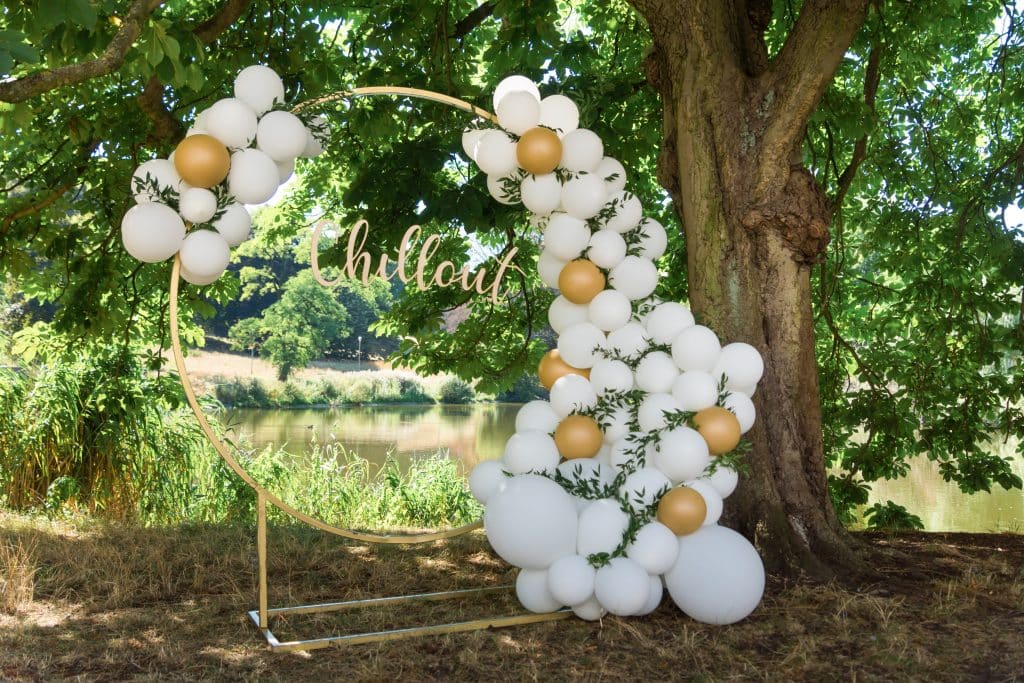 circular balloon arrangement with white and gold balloons with greenery next to tree with leaves